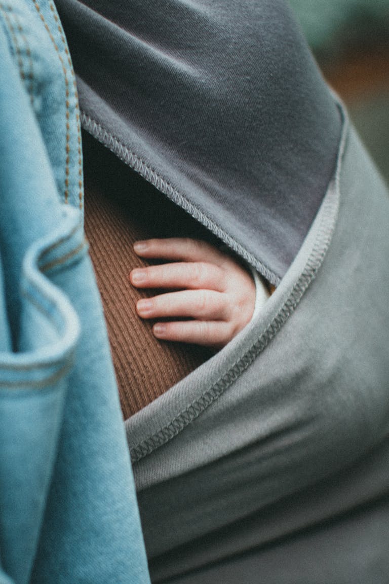 A baby's hand gently rests outside a cozy sling, symbolizing warmth and care.