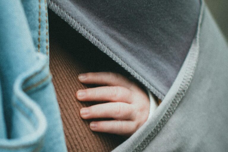 A baby's hand gently rests outside a cozy sling, symbolizing warmth and care.
