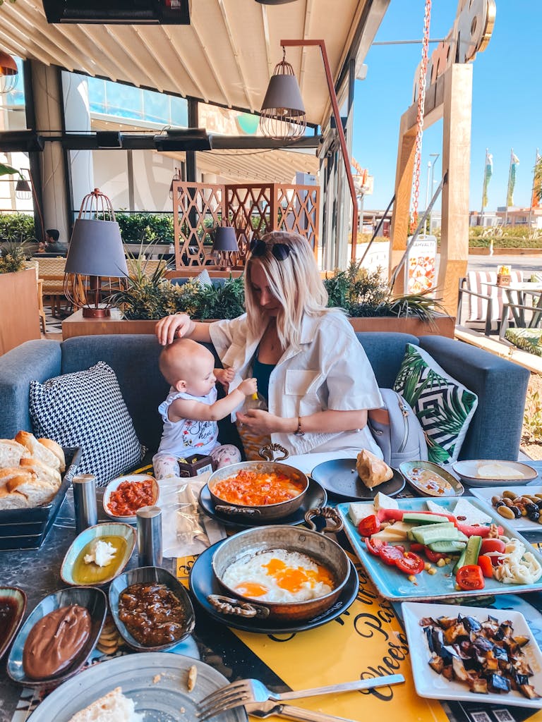 A mother feeds her baby in an outdoor café in İzmir with a table full of Turkish dishes.