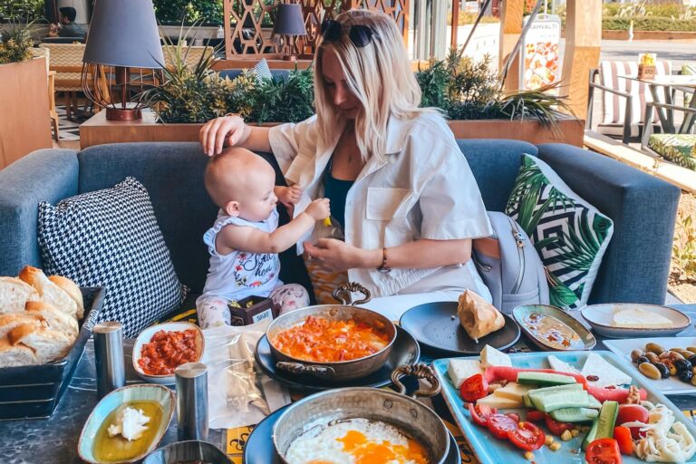 A mother feeds her baby in an outdoor café in İzmir with a table full of Turkish dishes.