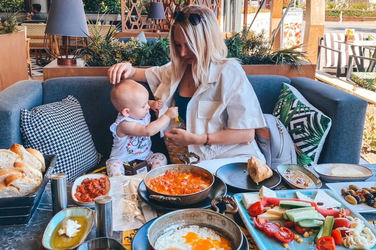 A mother feeds her baby in an outdoor café in İzmir with a table full of Turkish dishes.