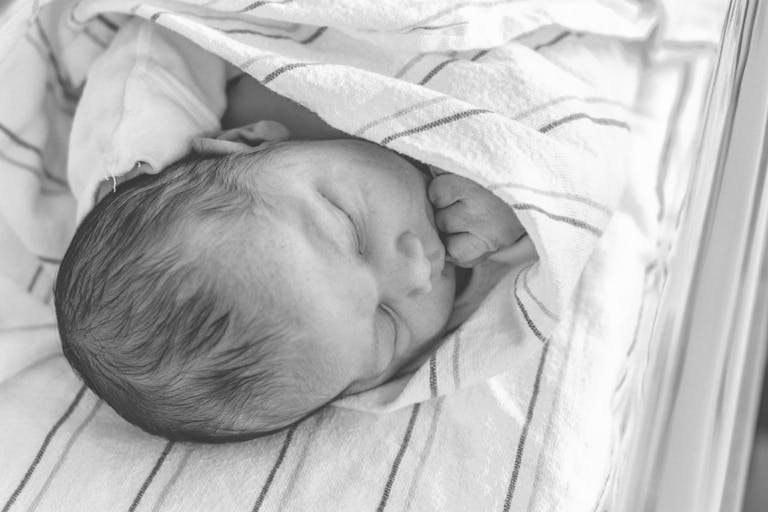 A serene black and white photo of a newborn baby sleeping peacefully, wrapped in a soft blanket.