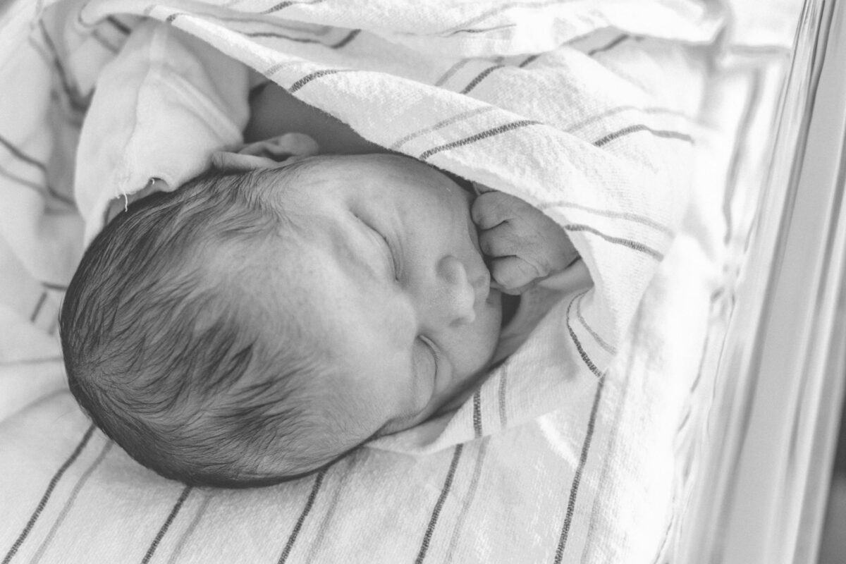 A serene black and white photo of a newborn baby sleeping peacefully, wrapped in a soft blanket. The swaddle blanket scam.