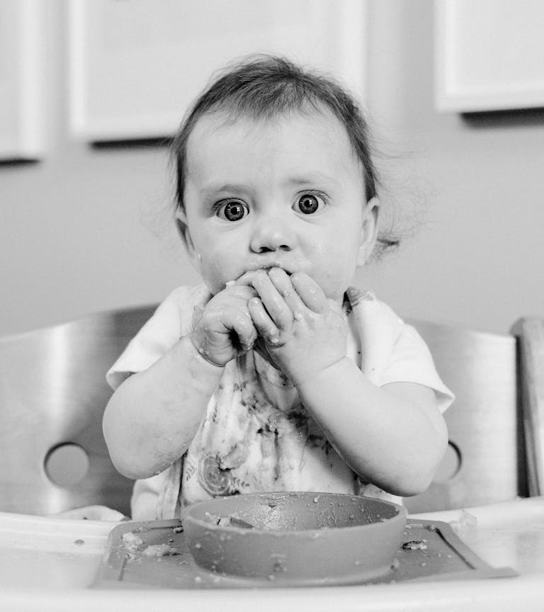 A black and white image capturing a baby's messy mealtime while eating.
