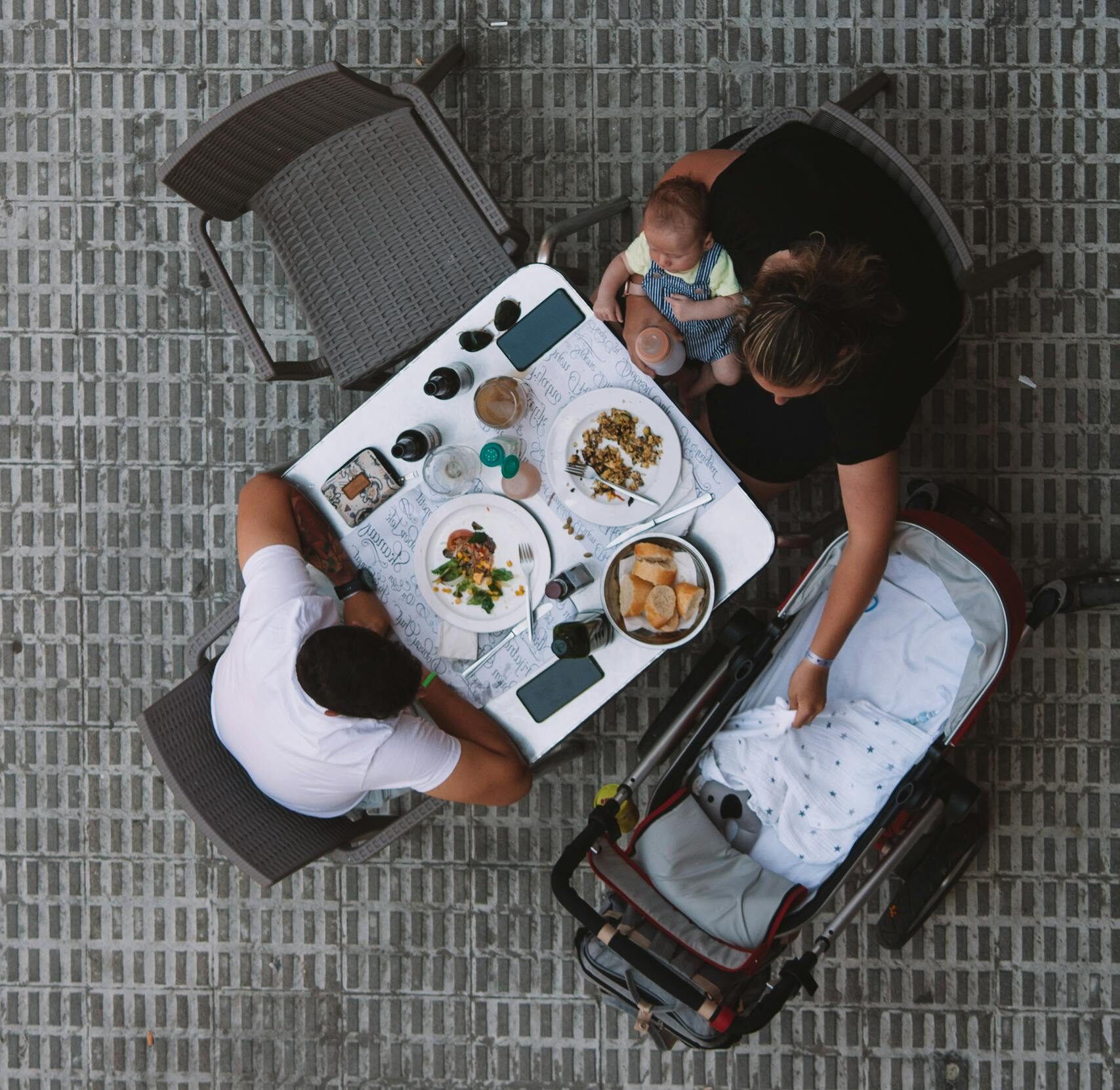 Dining Out with baby, A family enjoys a meal at an outdoor restaurant table, viewed from above with a baby in a stroller.