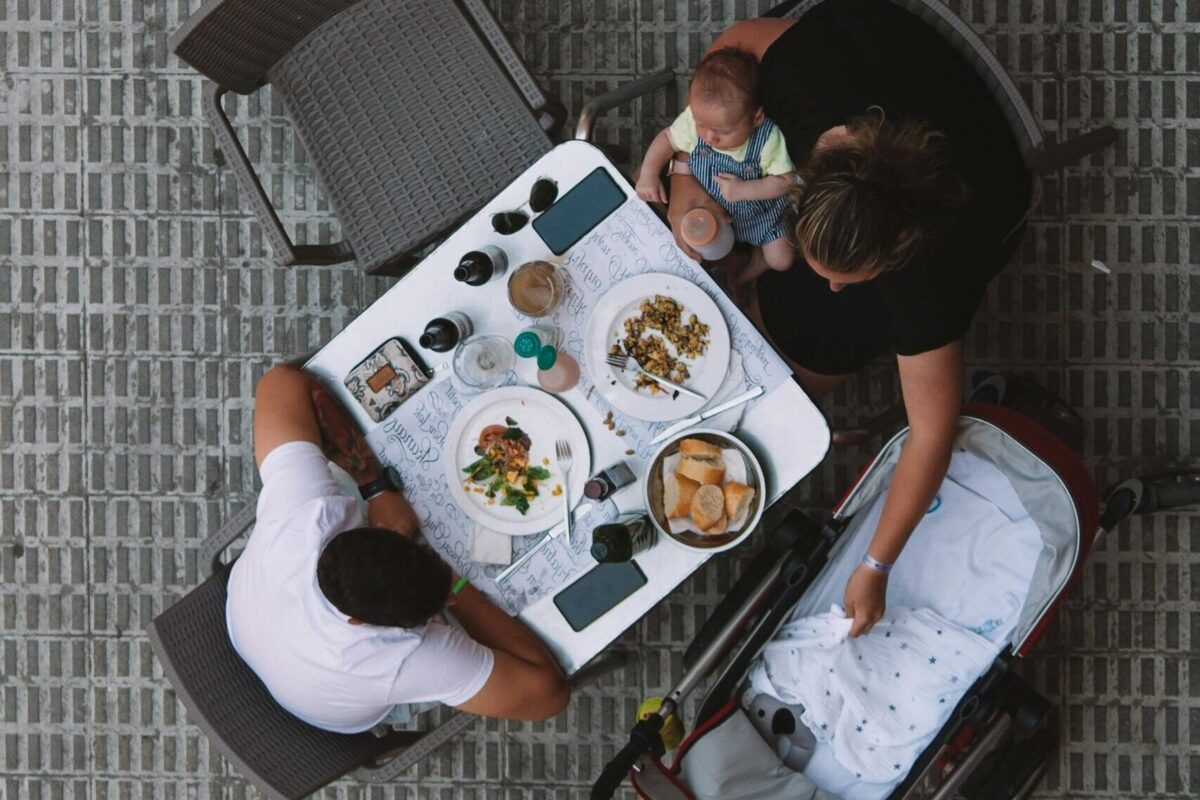Dining Out with baby, A family enjoys a meal at an outdoor restaurant table, viewed from above with a baby in a stroller. babies in public