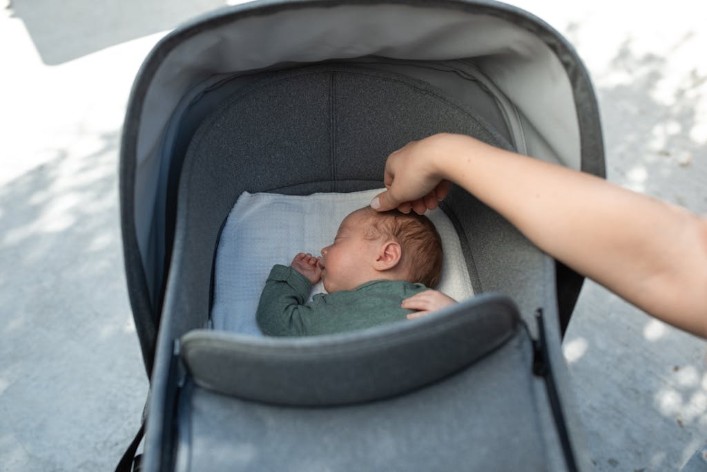 A serene moment of a baby sleeping in a stroller systems bassinet with a gentle touch from an adult hand.