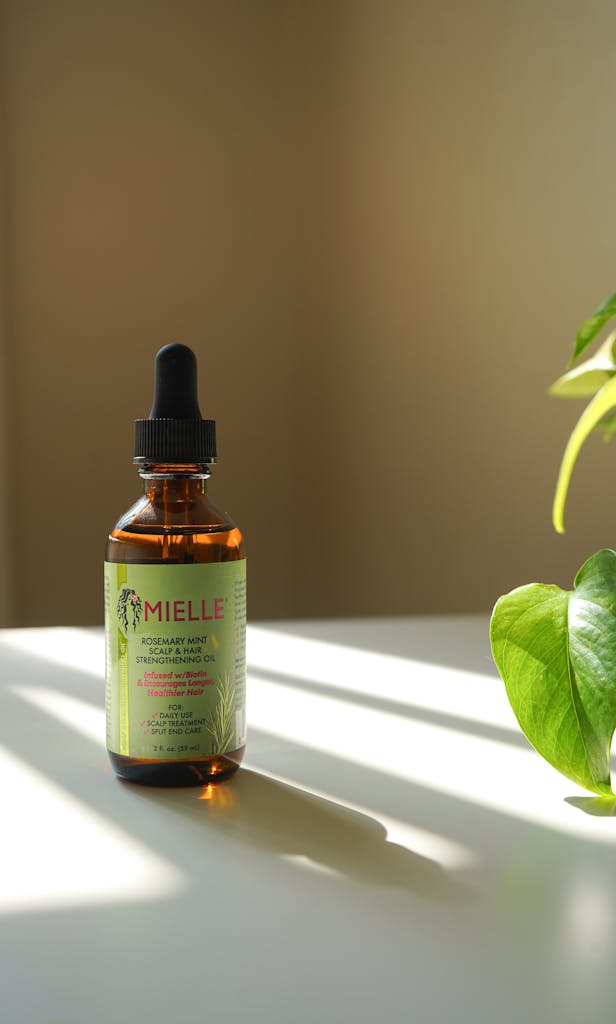 Amber glass bottle of essential oil with plant, sunlight casts shadows indoors. postpartum glow-up