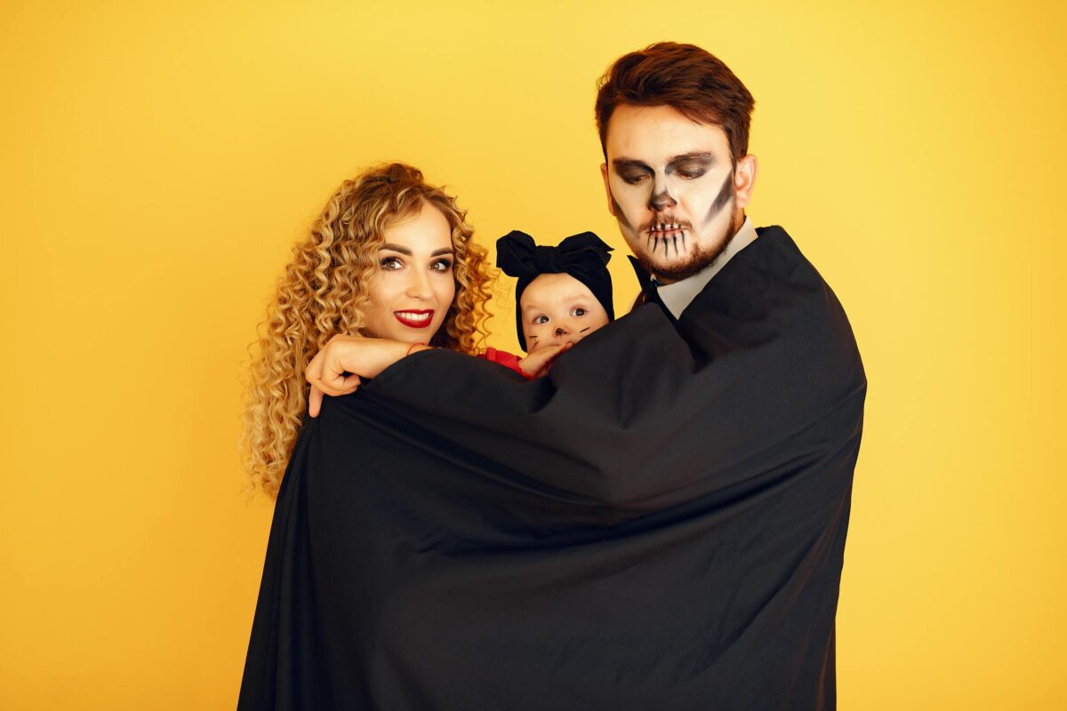 baby halloween costume: Family dressed in Halloween costumes posing together against a vibrant yellow background.