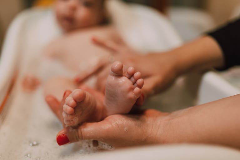 Bath time essentials Close-up of a baby's feet during a bath, with an adult's hands gently holding them.