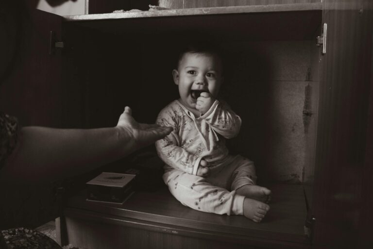 babyproofing: Charming grayscale photo of a baby sitting inside a cabinet, reaching out to a hand.