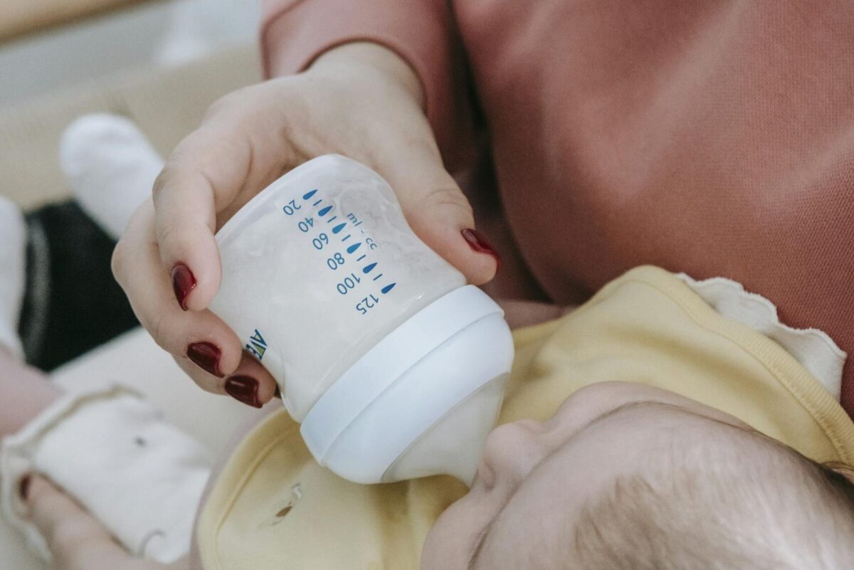 Closeup of crop anonymous female with cute little baby in hands sitting on bed