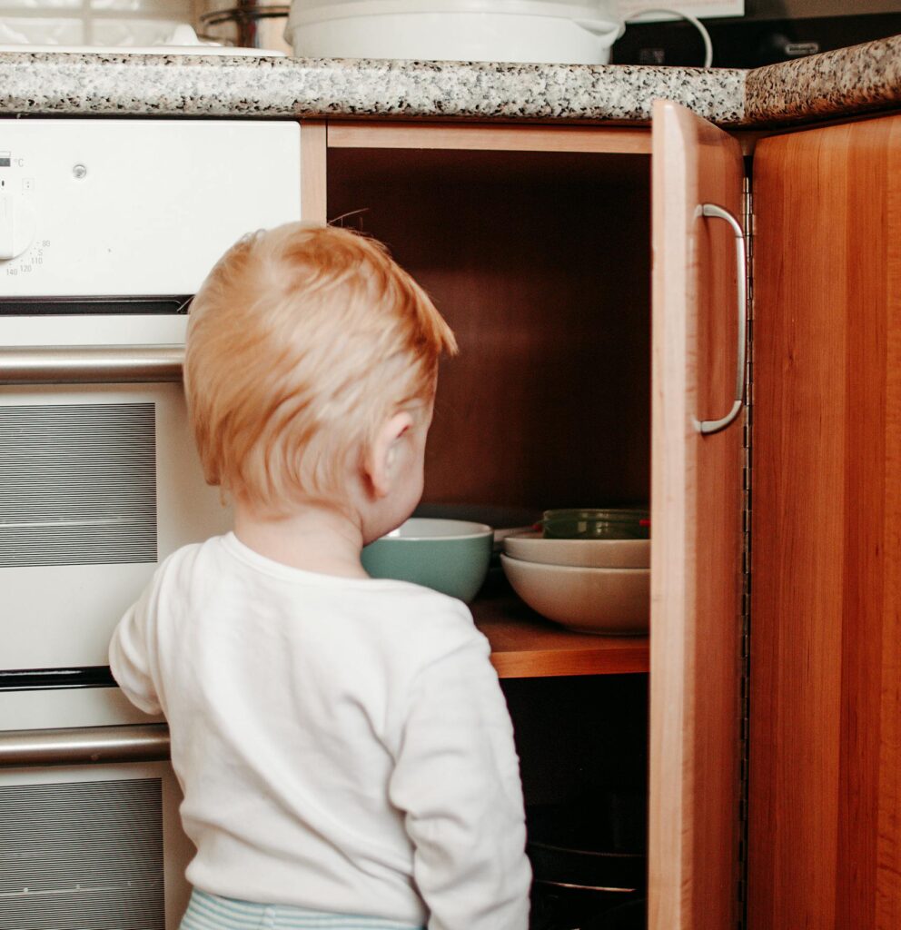 babyproofing: Curious toddler exploring kitchen cabinet, reaching for bowls. Captures innocence and exploration.