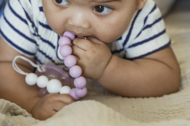 Cute little African American baby with curly hair lying on sofa while playing with beads in room on blurred background teething