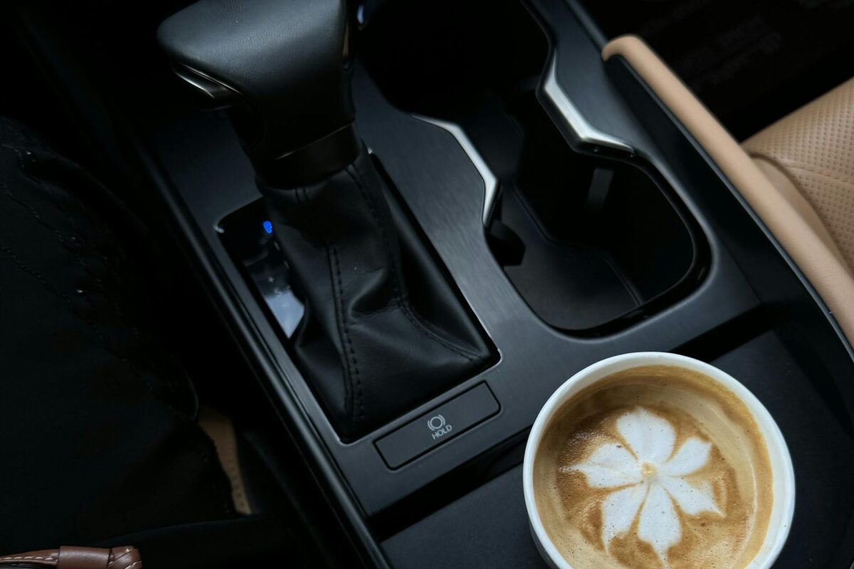mom car essentials: Latte with floral art placed in car's cup holder, brown leather wallet nearby.