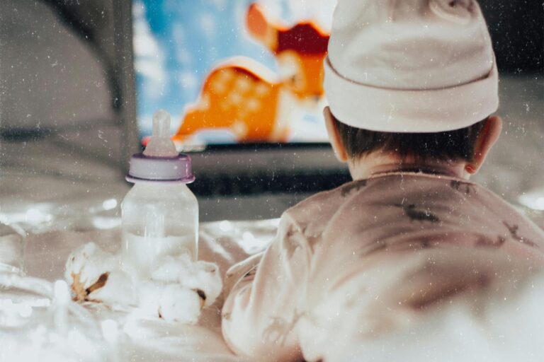 screen time for babies: A baby in pajamas watches an animated movie on a laptop, surrounded by soft lights and a bottle.