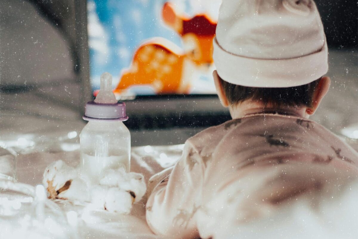 screen time for babies: A baby in pajamas watches an animated movie on a laptop, surrounded by soft lights and a bottle.