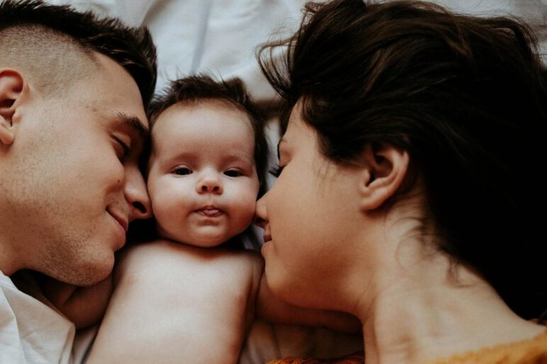 A family enjoys a warm, intimate moment lying on the bed with their baby co-sleeping