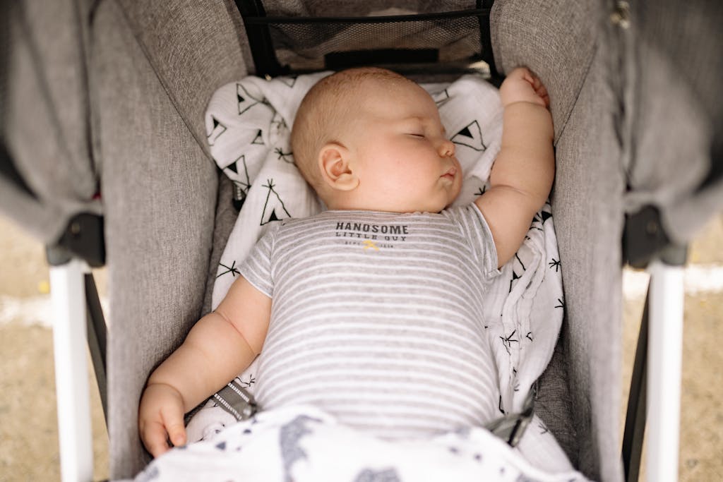 baby sleep schedules: Adorable baby peacefully sleeping in a stroller, wearing a striped onesie.