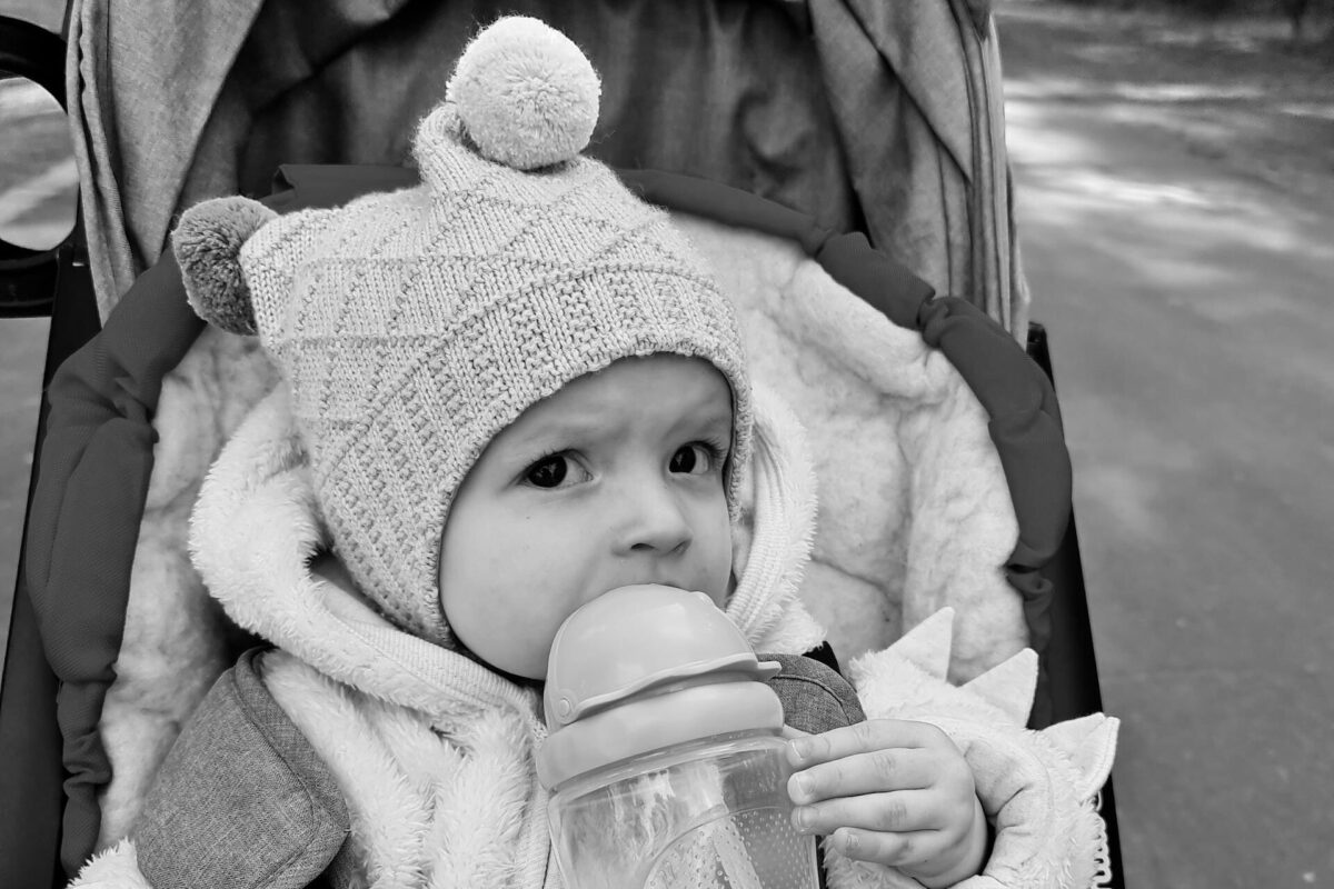Cute baby wearing winter clothing holds a sippy cup in a stroller during a stroll. Best sippy cup for six month old