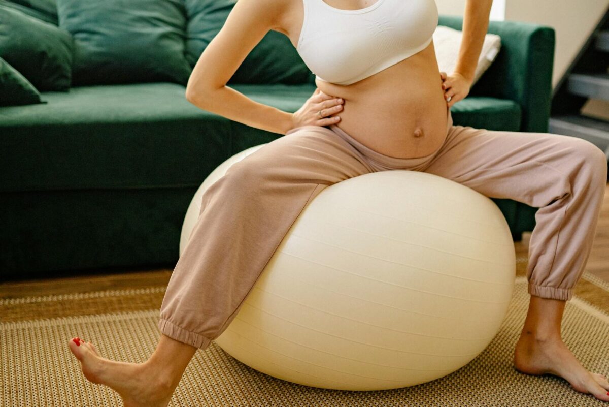labor hacks: Expectant mother enjoying a fitness routine indoors on a yoga ball.