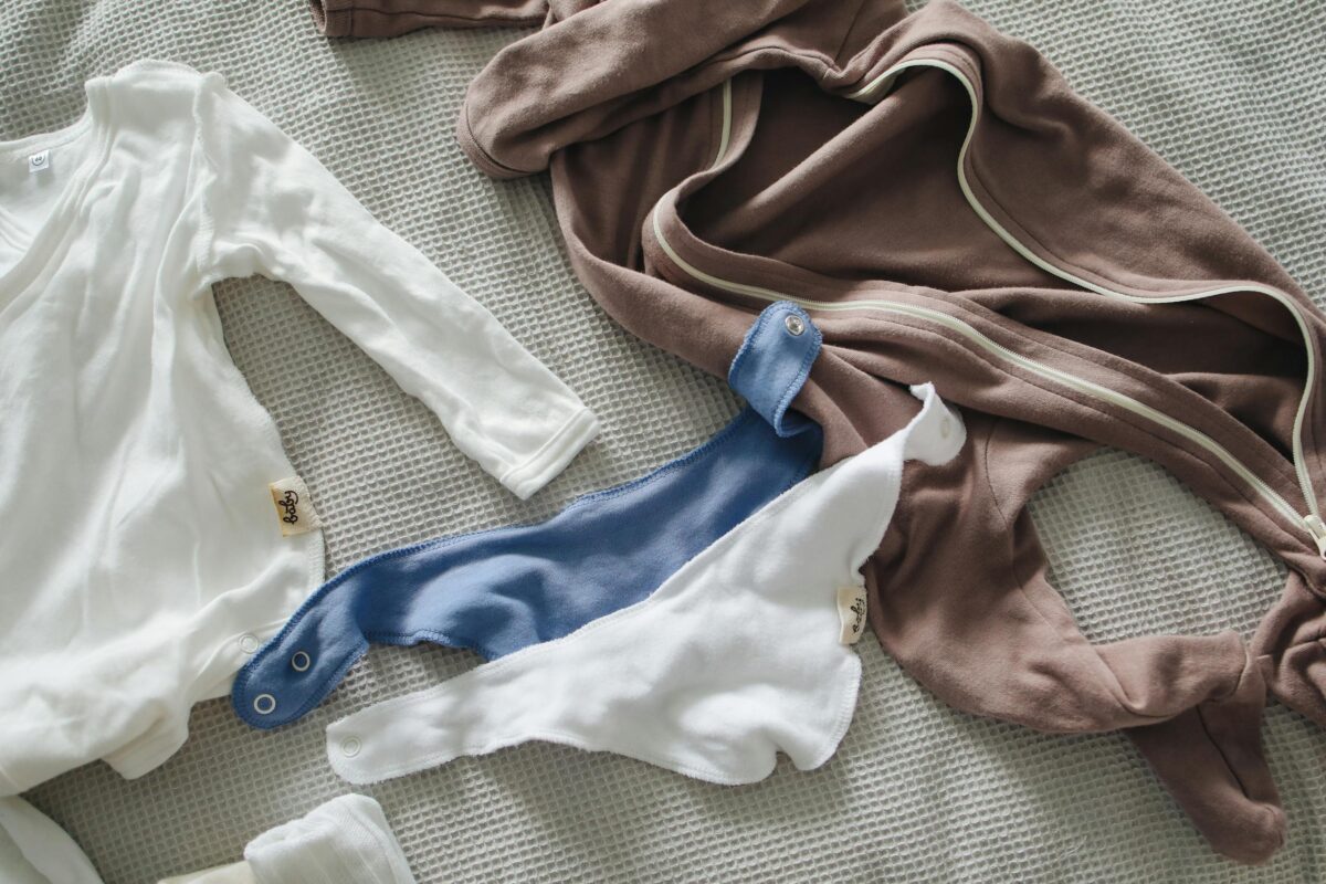 Ultimate nesting checklist: From above of small cotton suits and bibs for little babies on gray waffle bedspread on bed at home on daylight