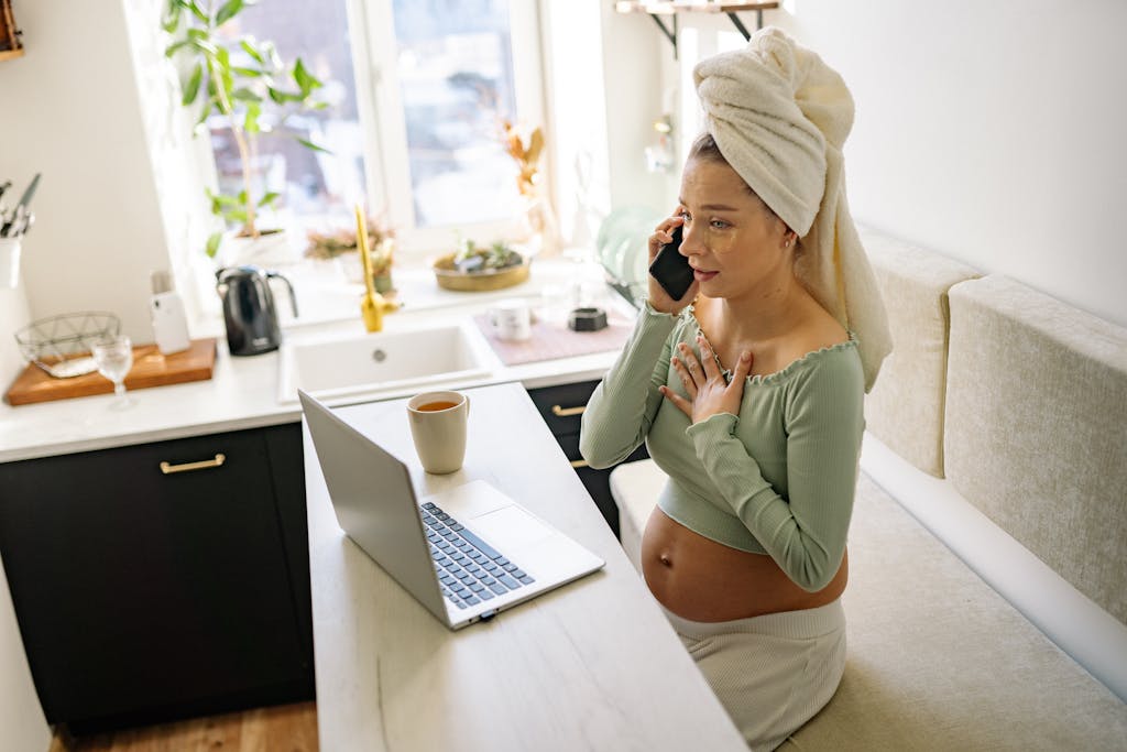 Pregnant woman in casual setting, talking on phone with laptop open and a drink nearby. Caffeine during pregnancy