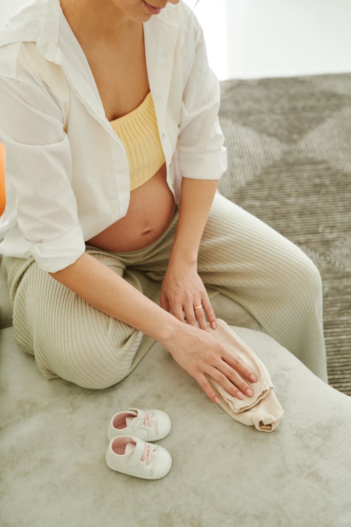 ultimate nesting checklist: Pregnant woman with baby shoes and clothing, reflecting anticipation and love.